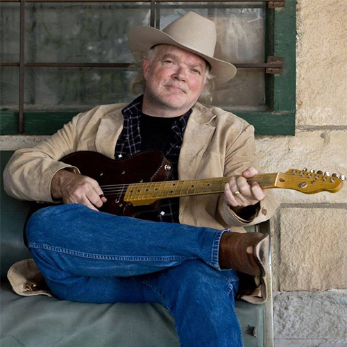 Image of Dallas Wayne sitting on a bench playing guitar