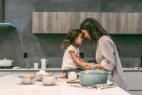 A smiling Mom and daughter touch foreheads in the kitchen